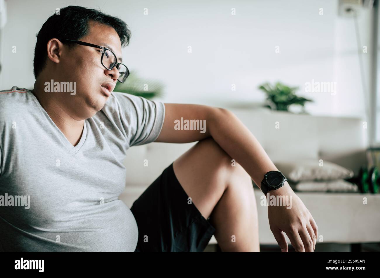 Lustiger übergewichtiger Mann, der erschöpft auf dem Boden sitzt, nach dem Workout mit Hantel, Kopierraum Stockfoto