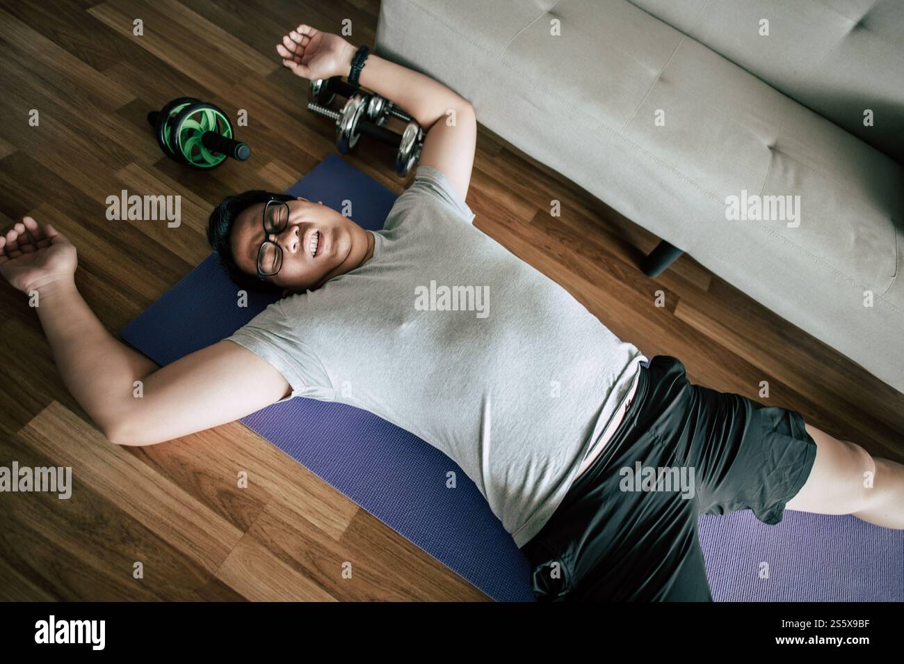 Lustiger übergewichtiger Mann in Brille schloss die Augen und lag erschöpft auf dem Boden nach dem Training, Kopierraum Stockfoto