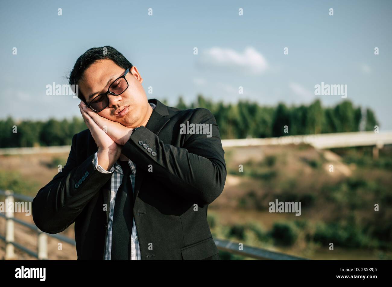 Junger asiatischer Geschäftsmann im Anzug mit Krawatte und Brille schließt seine Augen mit müde und schlafend, um sich im Freien zu entspannen Stockfoto