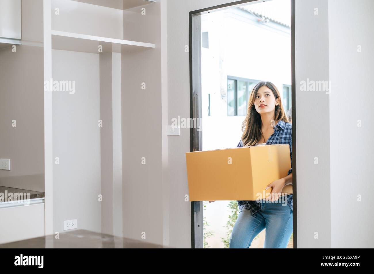 Junge asiatische Frau, die ein großes Paket trägt, geht in ein neues Haus mit einem glücklichen neuen Konzept Stockfoto