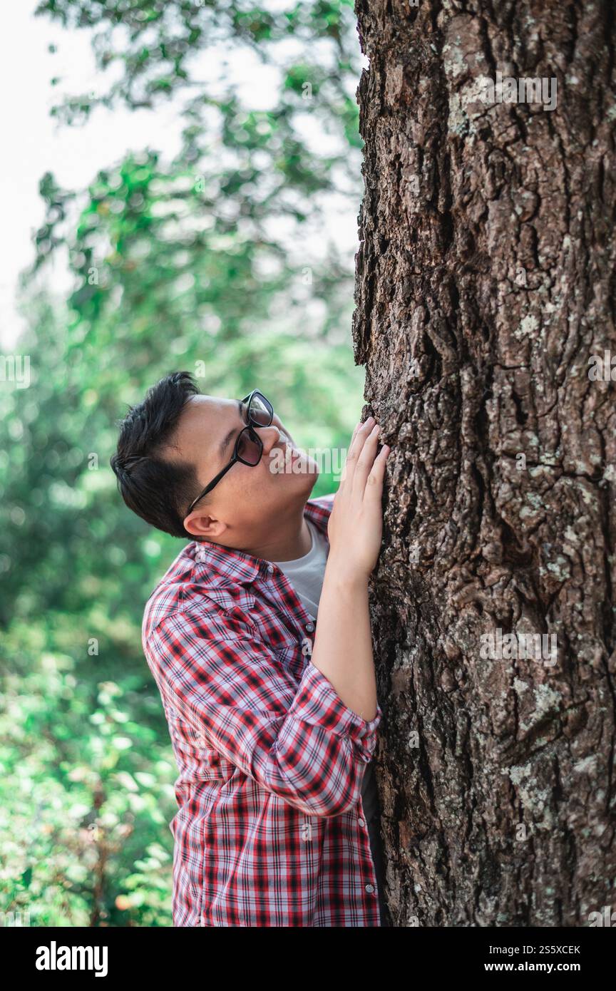 Porträt eines glücklichen asiatischen Mannes, der einen Baum im Wald umarmt. Die Natur schützen und lieben. Umwelt- und Umweltkonzept. Stockfoto