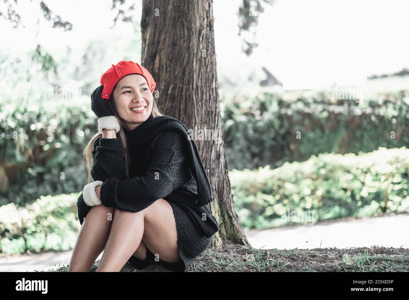 Porträt einer glücklichen asiatischen jungen Frau, die auf einem Rasen unter einem Baum im Park sitzt. Konzept der Umweltpflege. Stockfoto