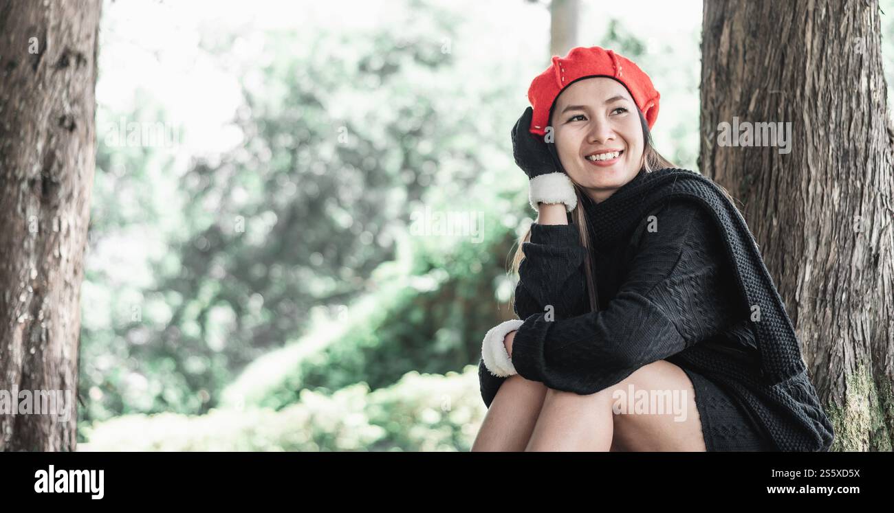 Porträt einer glücklichen asiatischen jungen Frau, die auf einem Rasen unter einem Baum im Park sitzt. Konzept der Umweltpflege. Stockfoto