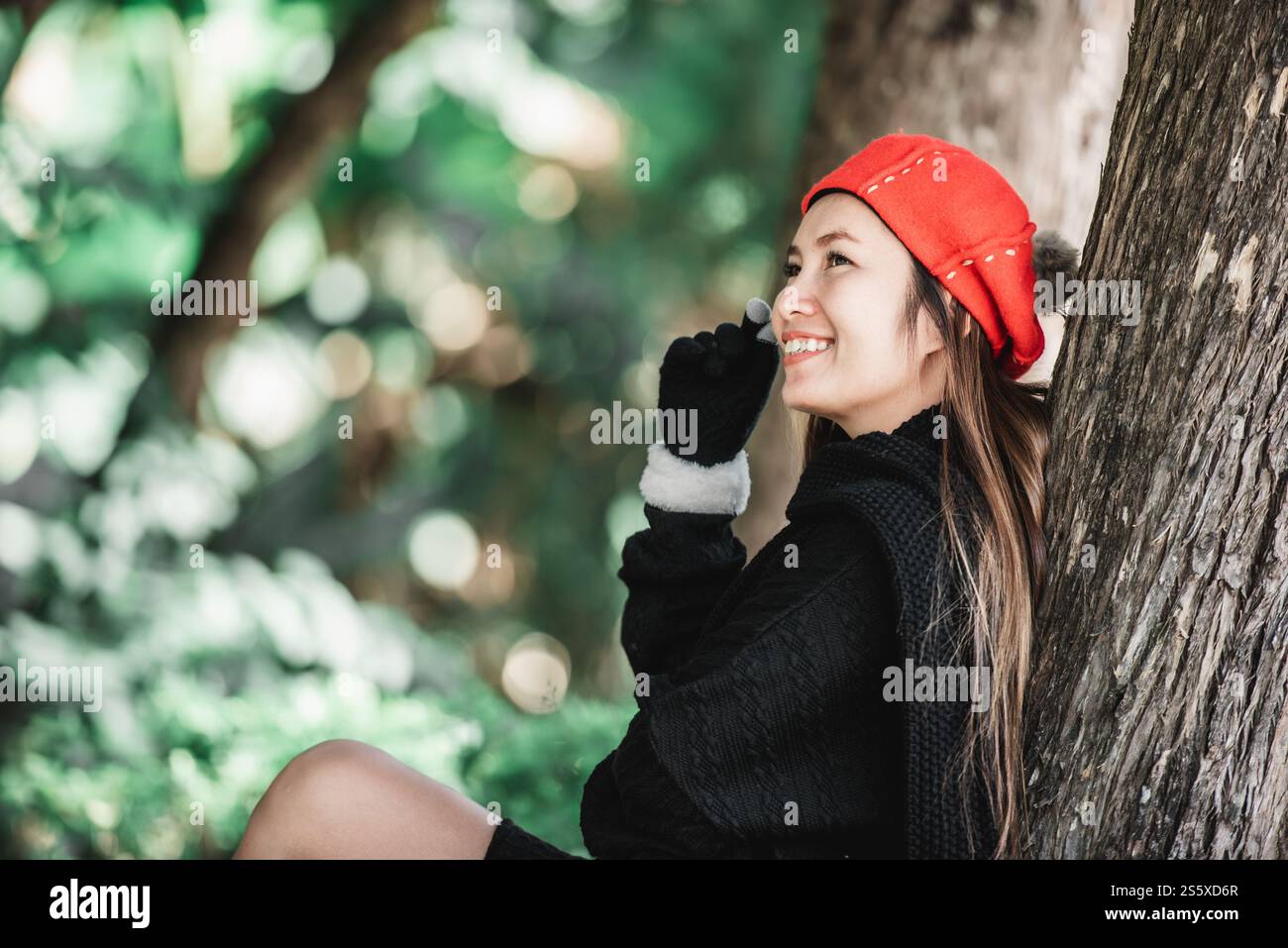 Porträt einer glücklichen asiatischen jungen Frau, die auf einem Rasen unter einem Baum im Park sitzt. Konzept der Umweltpflege. Stockfoto