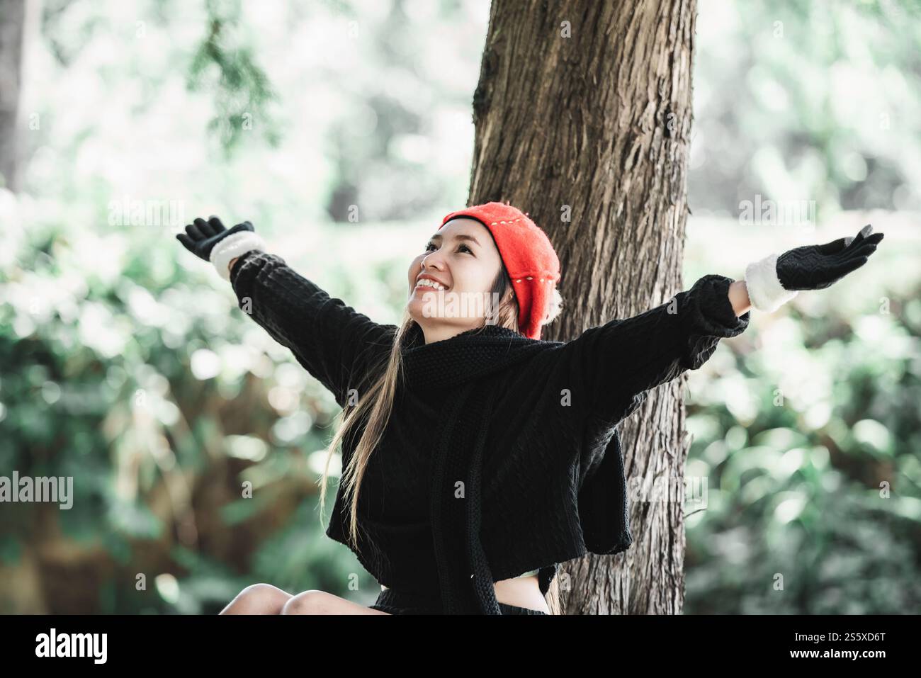 Porträt einer glücklichen asiatischen jungen Frau, die auf einem Rasen unter einem Baum im Park sitzt. Konzept der Umweltpflege. Stockfoto