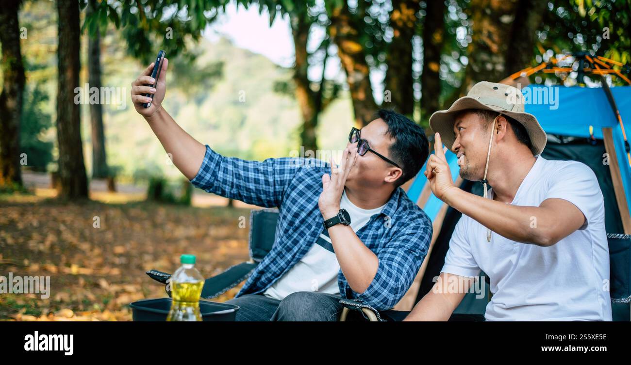 Porträt glücklicher asiatischer Mann Freunde, die einen Videoanruf mit Smartphone im Camping machen. Kochset vorne. Outdoor-Kochen, Reisen, Camping, Stockfoto