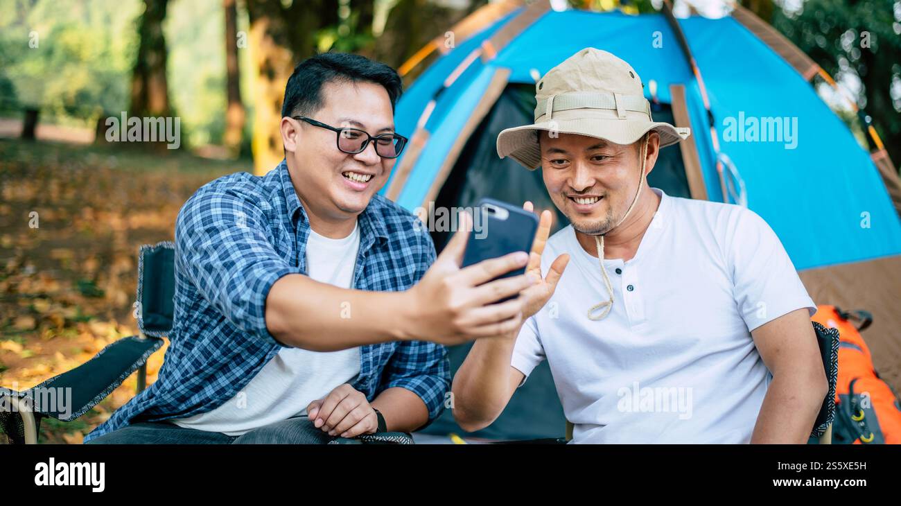 Porträt glücklicher asiatischer Mann Freunde, die einen Videoanruf mit Smartphone im Camping machen. Kochset vorne. Outdoor-Kochen, Reisen, Camping, Stockfoto