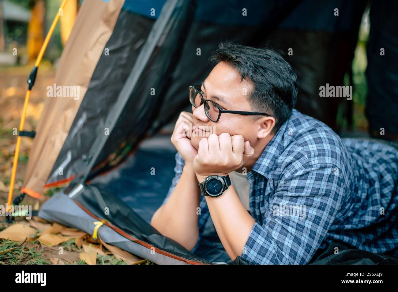 Porträt einer glücklichen Brille des asiatischen Reisenden, die im Zeltcamping liegt. Outdoor-Reisen, Camping und Lifestyle-Konzept. Stockfoto