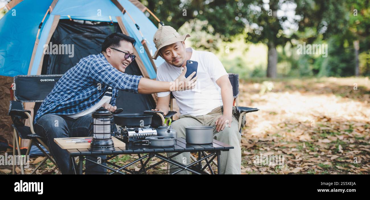 Porträt glücklicher asiatischer Mann Freunde, die einen Videoanruf mit Smartphone im Camping machen. Kochset vorne. Outdoor-Kochen, Reisen, Camping, Stockfoto