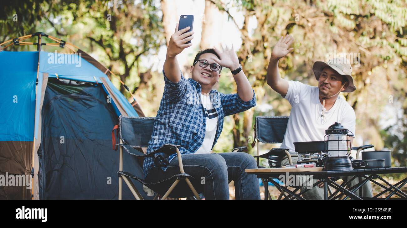 Porträt glücklicher asiatischer Mann Freunde, die einen Videoanruf mit Smartphone im Camping machen. Kochset vorne. Outdoor-Kochen, Reisen, Camping, Stockfoto