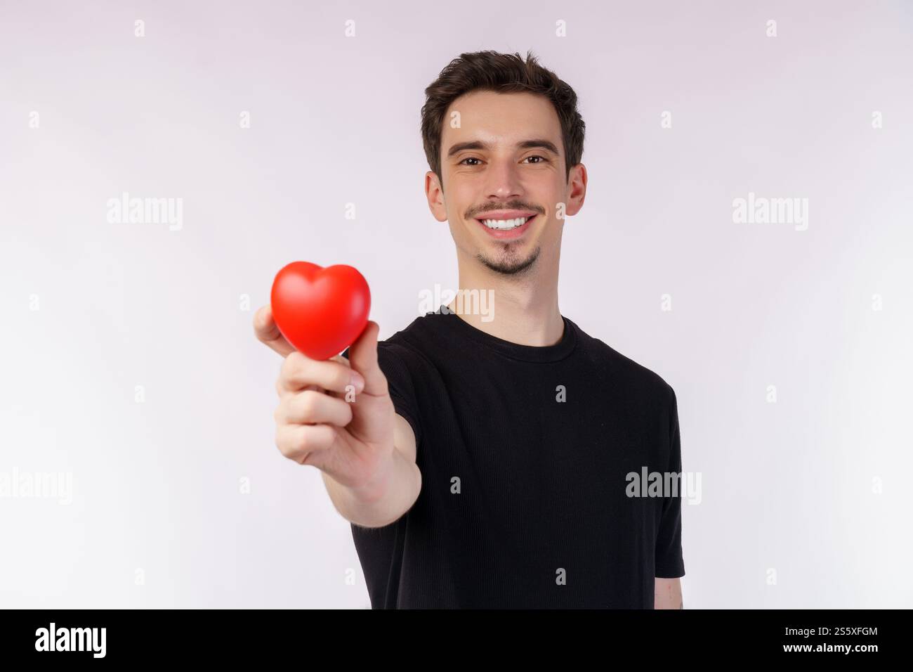 Porträt eines glücklichen jungen kaukasischen Mannes, der ein schwarzes T-Shirt trägt, hält einen roten Apfel auf isoliertem Hintergrund. Ernährung, Gesundheit, gesunde Ernährung Stockfoto