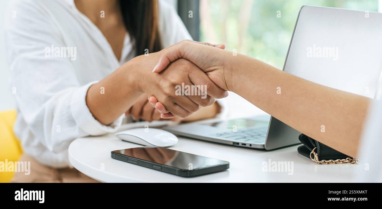 Selektiver Fokus auf zwei Geschäftsfrauen, die sich über einen Schreibtisch mit Laptop bewegen, als Abschluss eines Geschäfts oder einer Partnerschaft im Café Stockfoto
