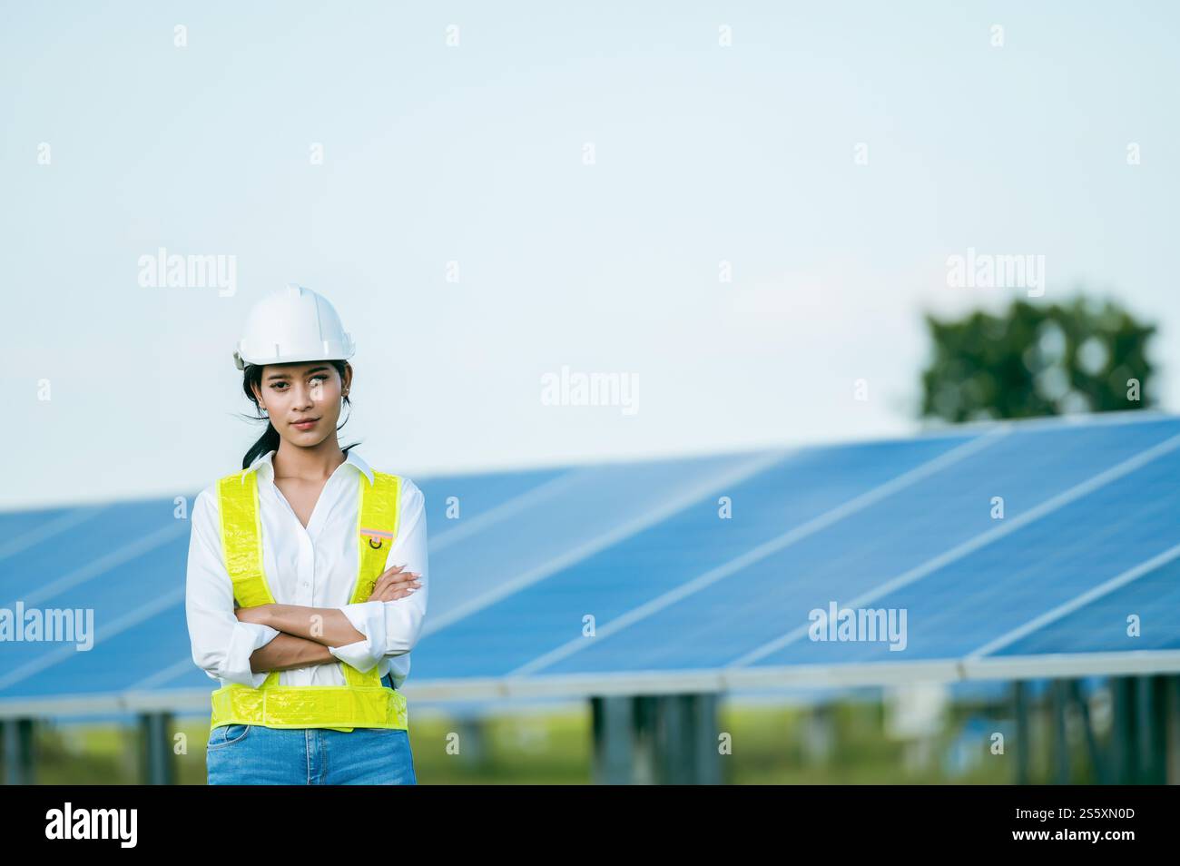 Portrait Asiatische junge Ingenieurin, die Schutzkleidung und Helm trägt, die vor dem Solarpanel steht, um die Operation in Papierkram zu überprüfen, während Stockfoto