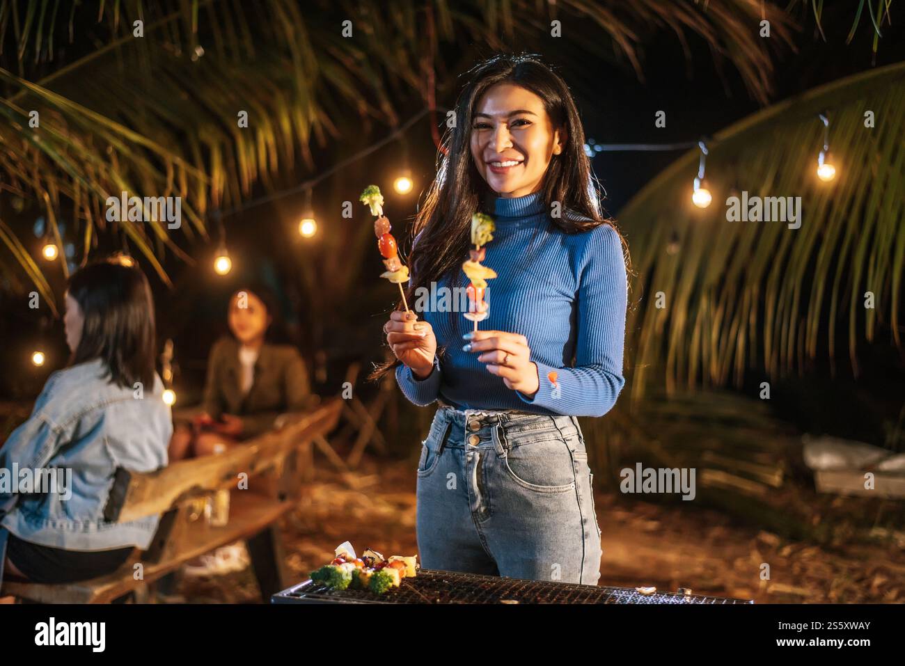 Porträt einer glücklichen asiatischen jungen Frau, die Fleisch auf dem Grill auf der Neujahrsfeier kocht. Bar-B-Q oder BBQ auf traditionellem Herd. Nachtparty, Leute und Stockfoto
