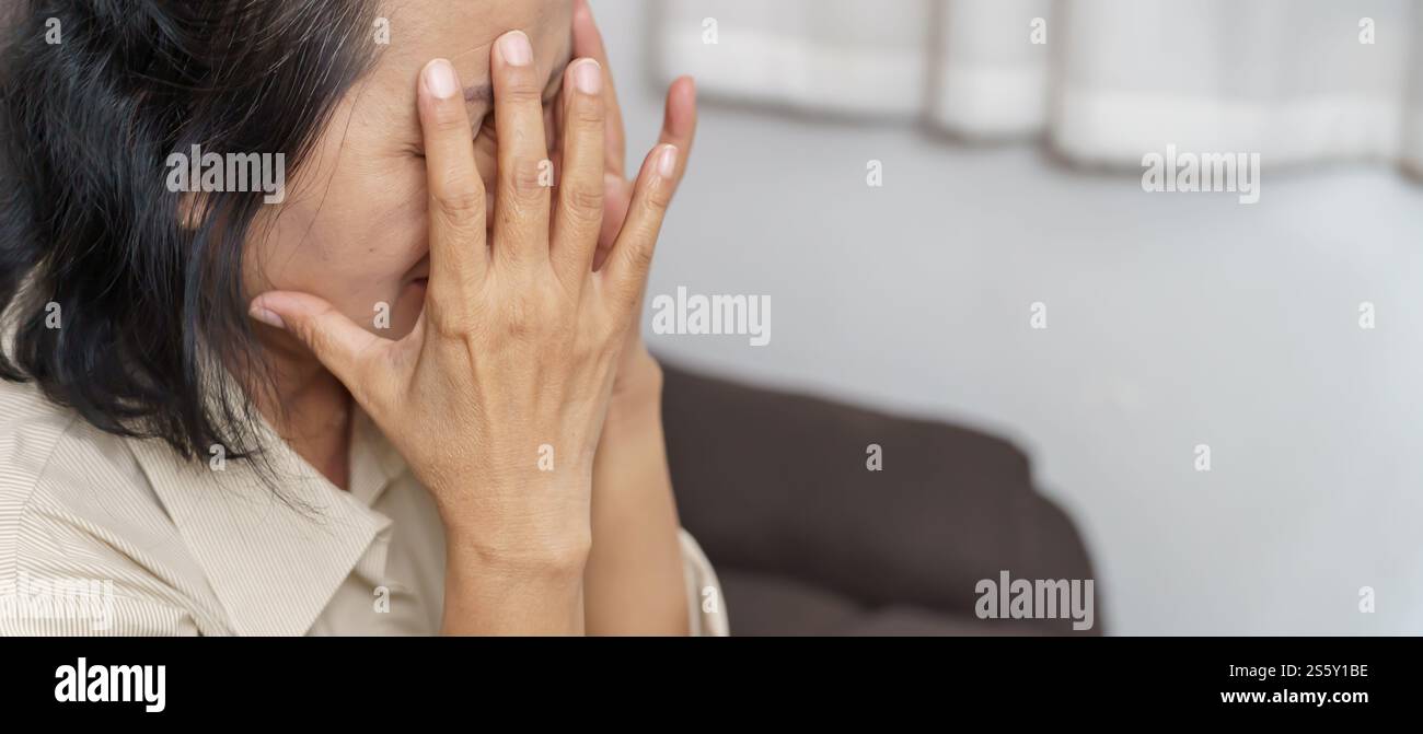 Traurige asiatische Frau mittleren Alters, die die Stirn berührt und Kopfschmerzen hat, die an Migräne leiden. Reife asiatische Frau, die krank oder depressiv ist Stockfoto