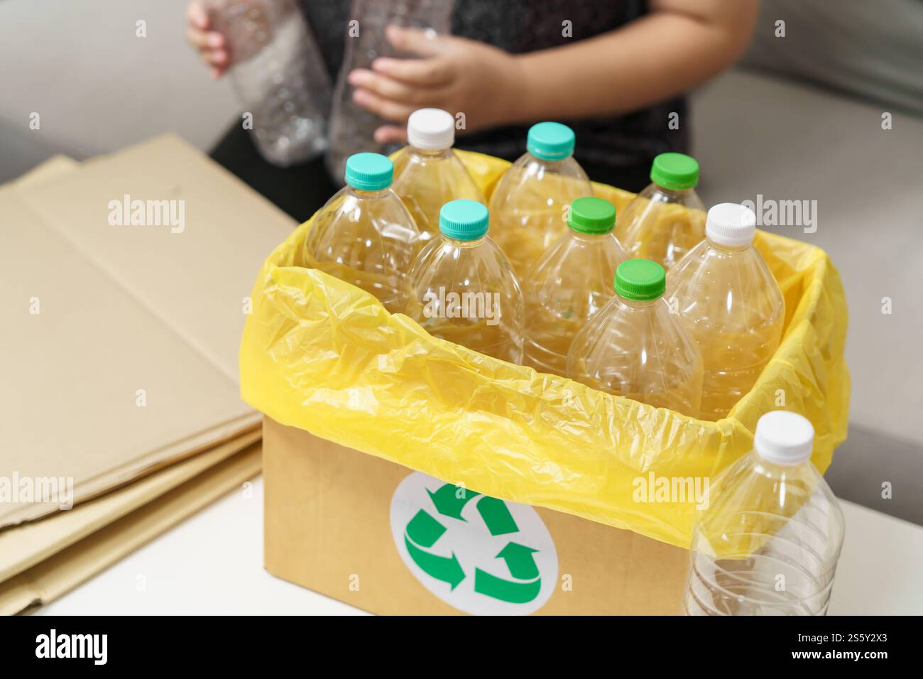 Recyceln Sie die umweltfreundliche Zero Concept Frau, die leere Plastikflasche mit gelben Mülltüten zu Hause in den Recyclingbehälter wirft Stockfoto