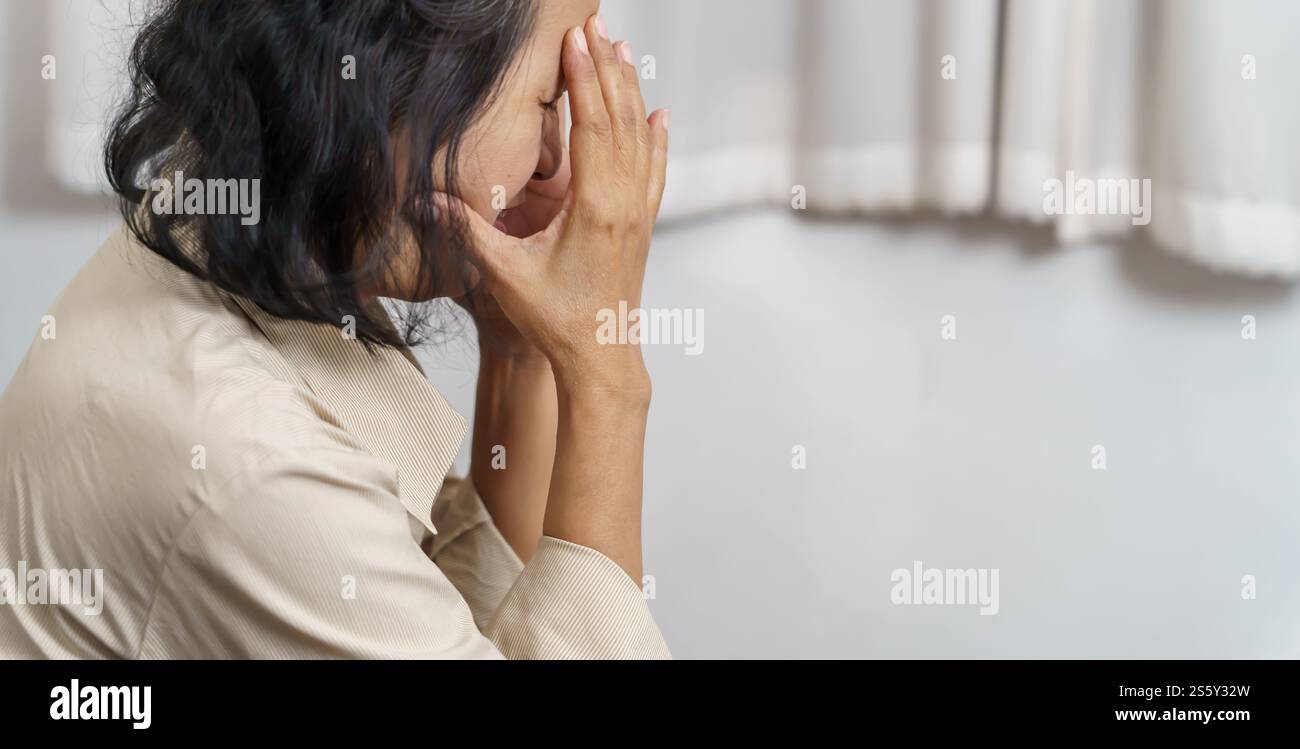 Traurige asiatische Frau mittleren Alters, die die Stirn berührt und Kopfschmerzen hat, die an Migräne leiden. Reife asiatische Frau, die krank oder depressiv ist Stockfoto