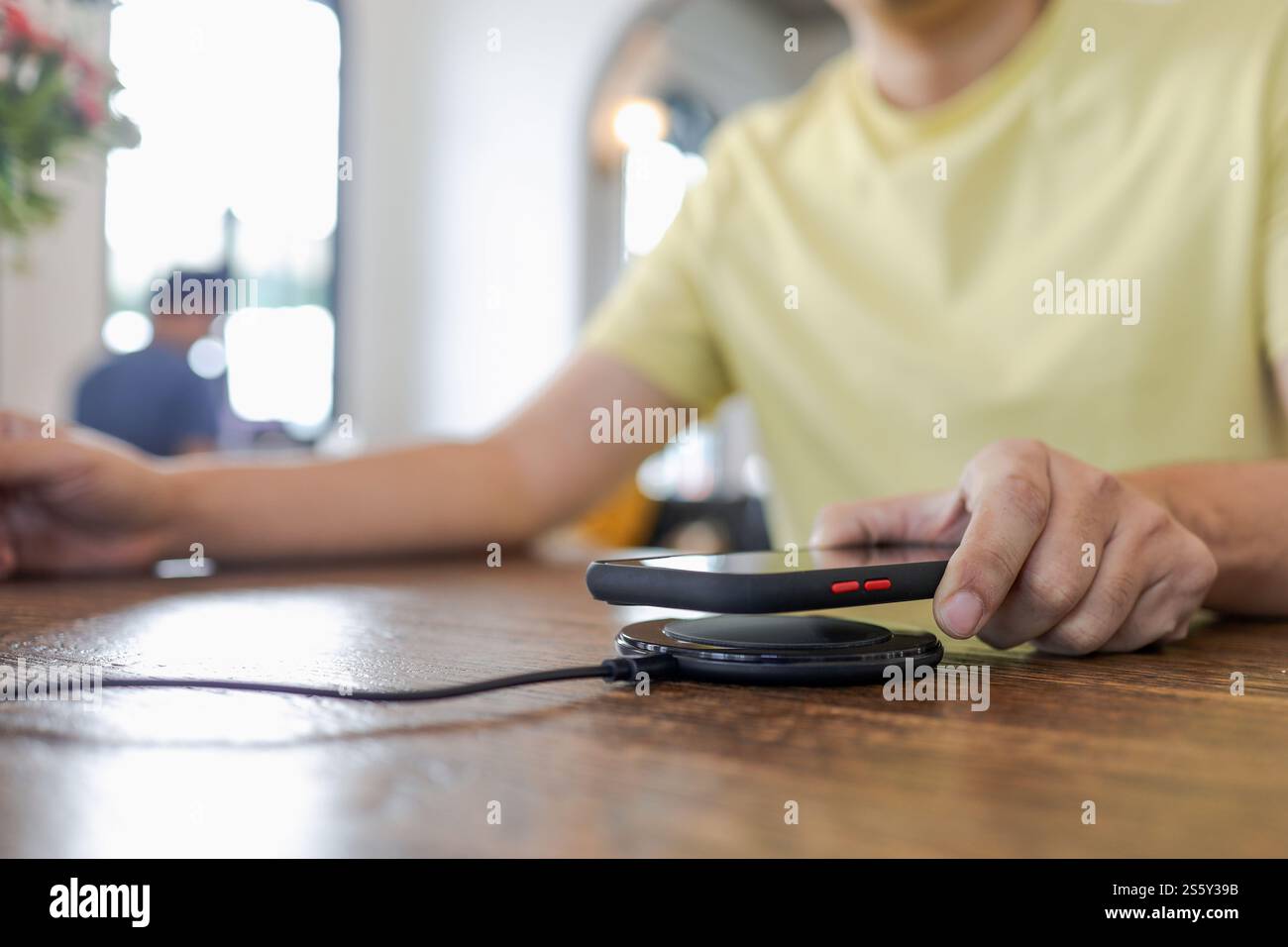 Laden des Mobiltelefonakkus mit dem drahtlosen Gerät in der Tabelle. Smartphone wird auf einem Ladepad aufgeladen. Mobiltelefon in der Nähe des kabellosen Ladegeräts Stockfoto