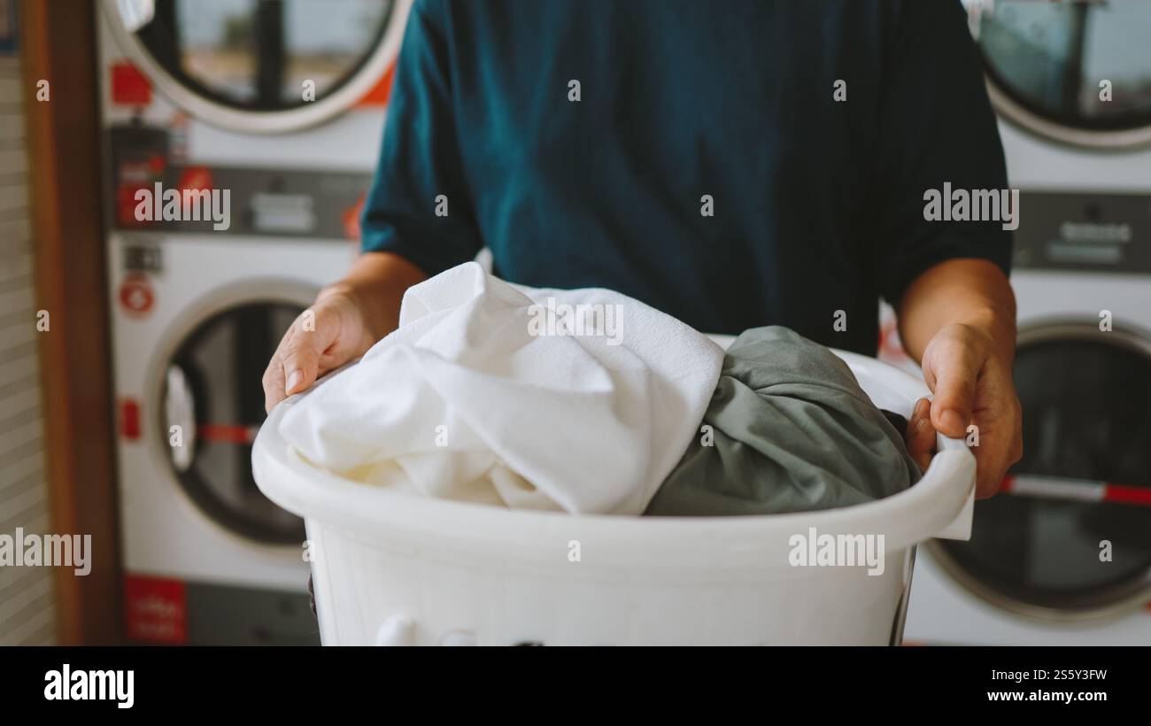 Hausmann mit Korb und schmutziger Wäsche gewaschene Kleidung im Waschraum. Waschmaschine im Wäschereigeschäft Konzept Stockfoto