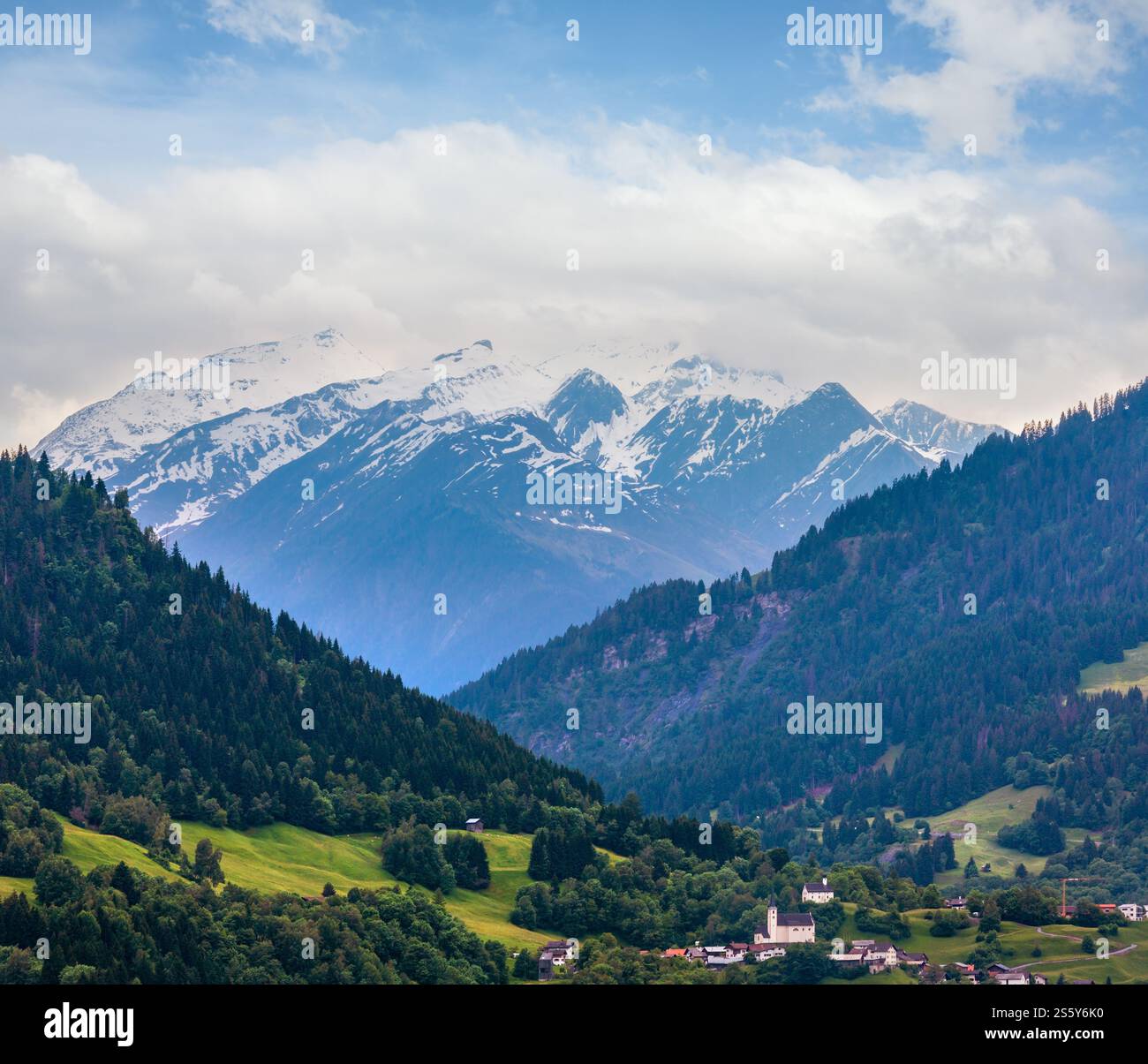 Sommer Alpen Berglandschaft mit Dorf, Tanne Wald am Hang und schneebedeckten Rocky tops in weit, Österreich. Stockfoto