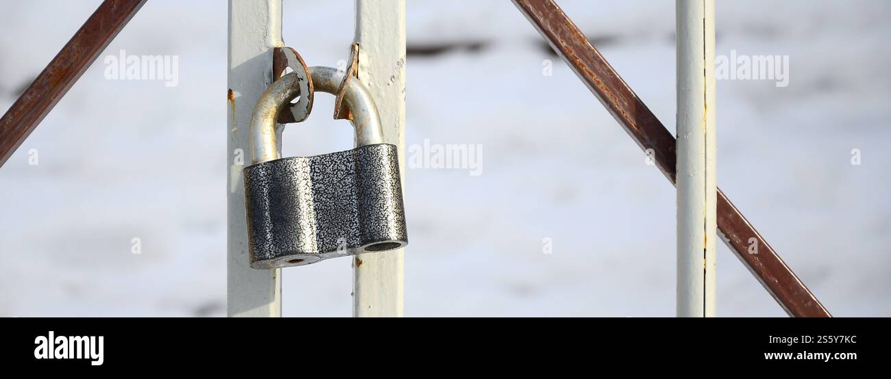 Ein großes graues Vorhängeschloss hängt an einem Metalltor Stockfoto