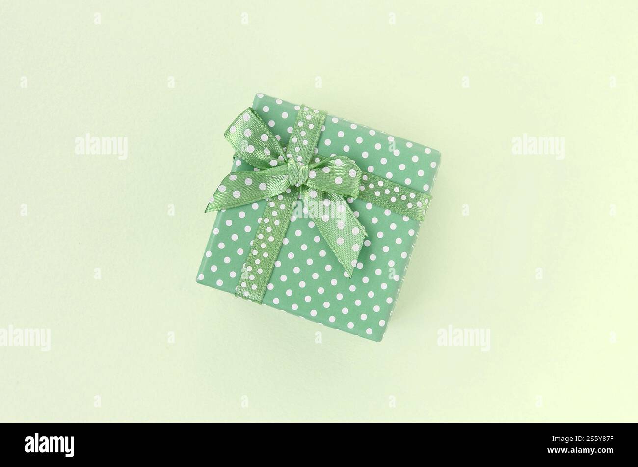Kleine grüne Geschenkbox mit Band liegt auf kalkfarbenem Hintergrund. Minimalistischer, flacher Blick von oben. Kleine grüne Geschenkbox mit Band liegt auf kalkfarbenem Hintergrund Stockfoto