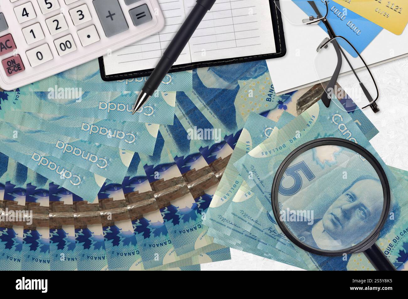 5 kanadische Dollarscheine und Taschenrechner mit Brille und Stift. Steuerzahlungssaisonkonzept oder Investitionslösungen. Job mit hohem Gehalt wird gesucht Stockfoto