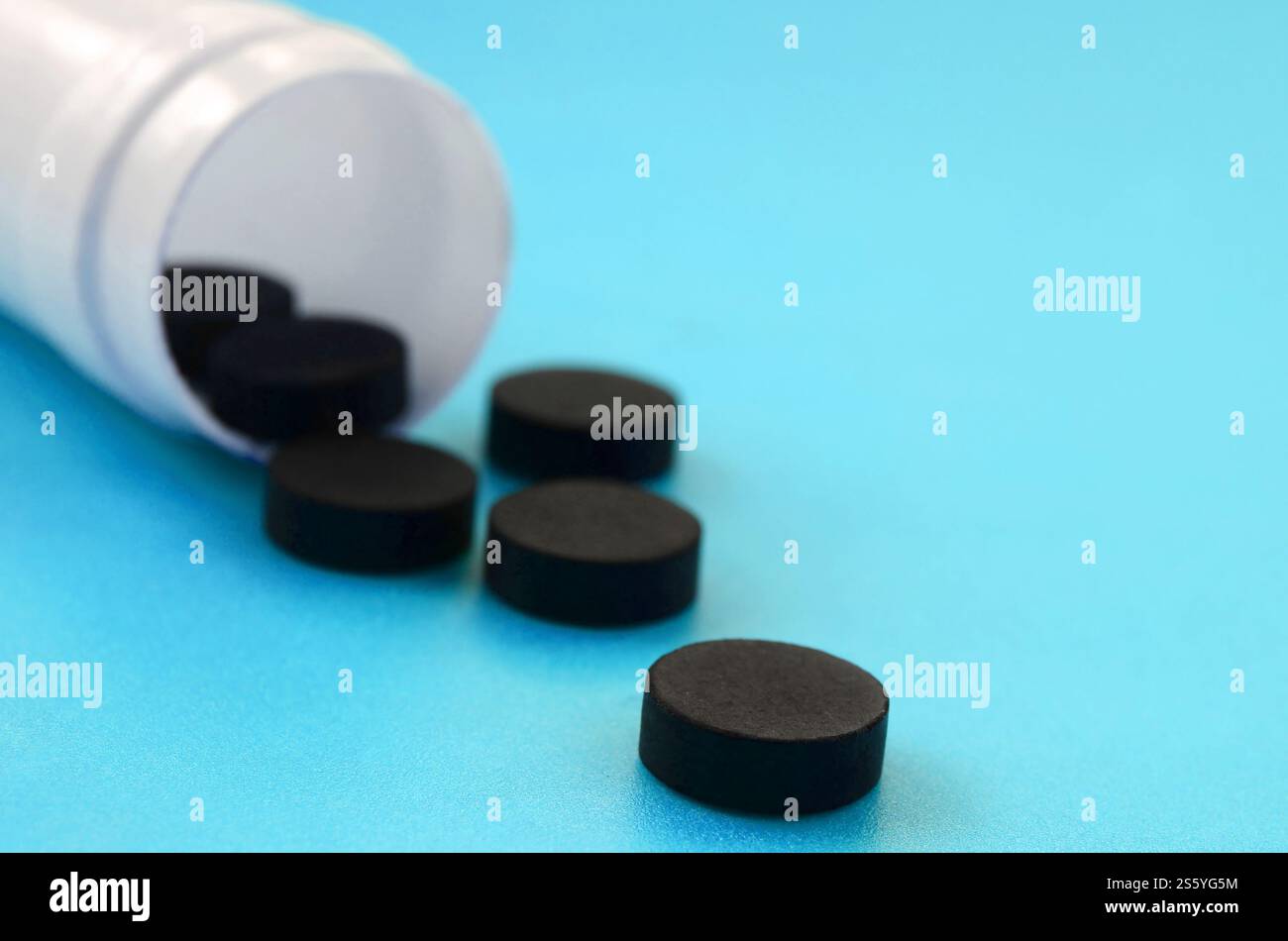 Mehrere schwarze Tabletten fallen aus der Kunststoffbehälter auf der blauen Fläche. Hintergrundbild über medizinische und pharmazeutische Themen. Aktivkohle Stockfoto