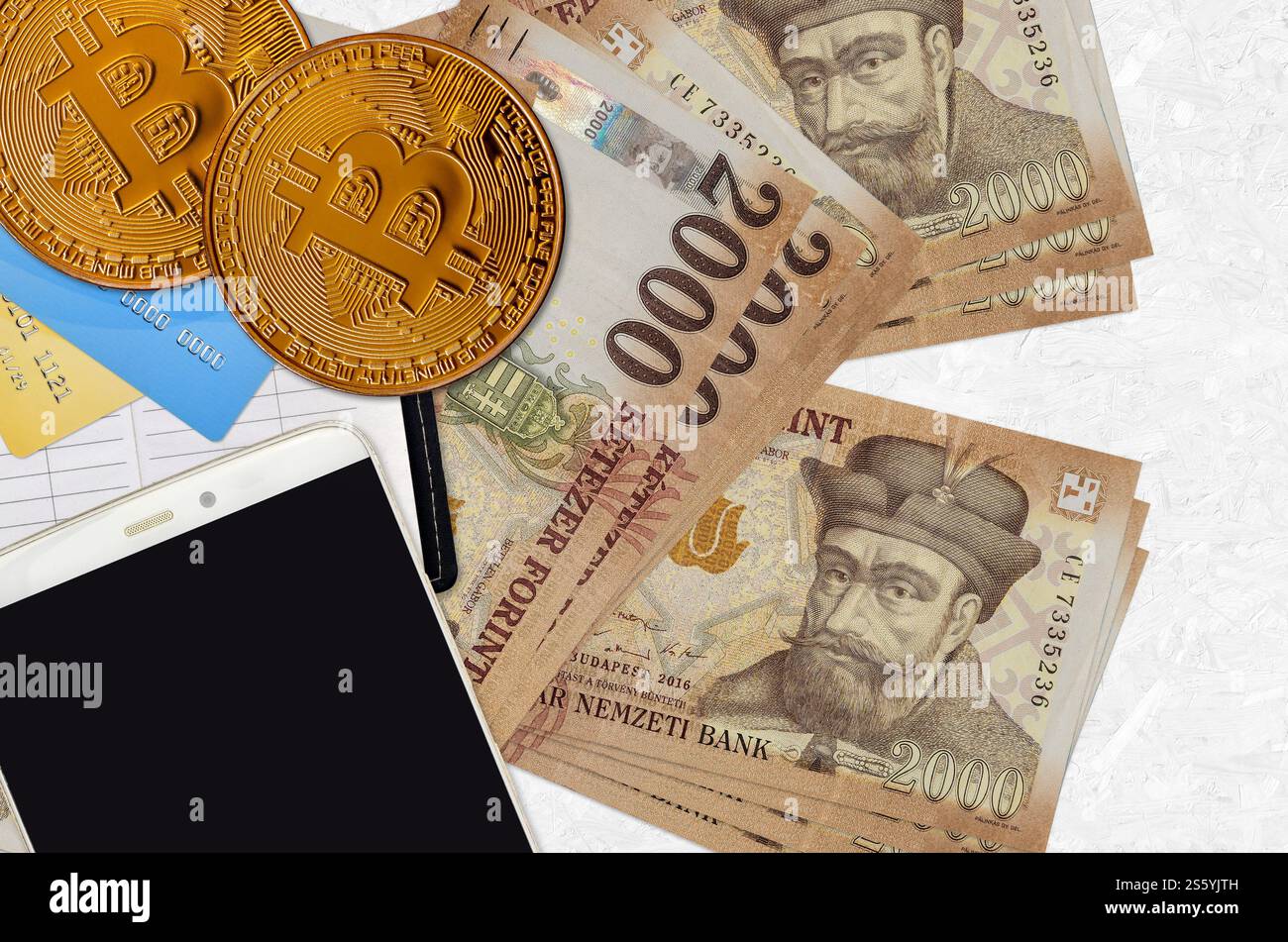 2000 ungarische Forint-Scheine und goldene Bitcoins mit Smartphone und Kreditkarten. Anlagekonzept für Kryptowährungen. Krypto-Mining oder -Handel Stockfoto