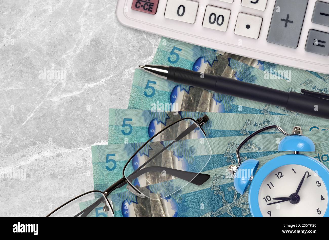 5 kanadische Dollarscheine und Taschenrechner mit Brille und Stift. Geschäftsdarlehen oder Steuerzahlung Saisonkonzept. Finanzplanung und Zeit für die Zahlung von Steuern. Stockfoto