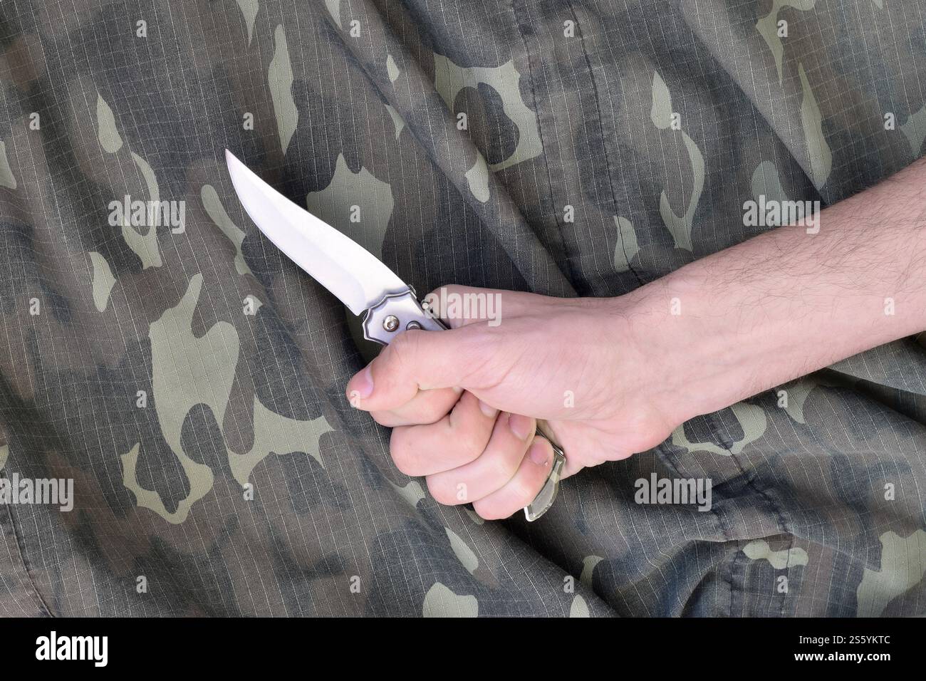 Hand mit kleinem Messer auf Tarnstoff Hintergrund. Das Konzept, ein Messer in Nahkampftaktiken beim Militär einzusetzen. Hand mit kleinem Messer auf Stockfoto