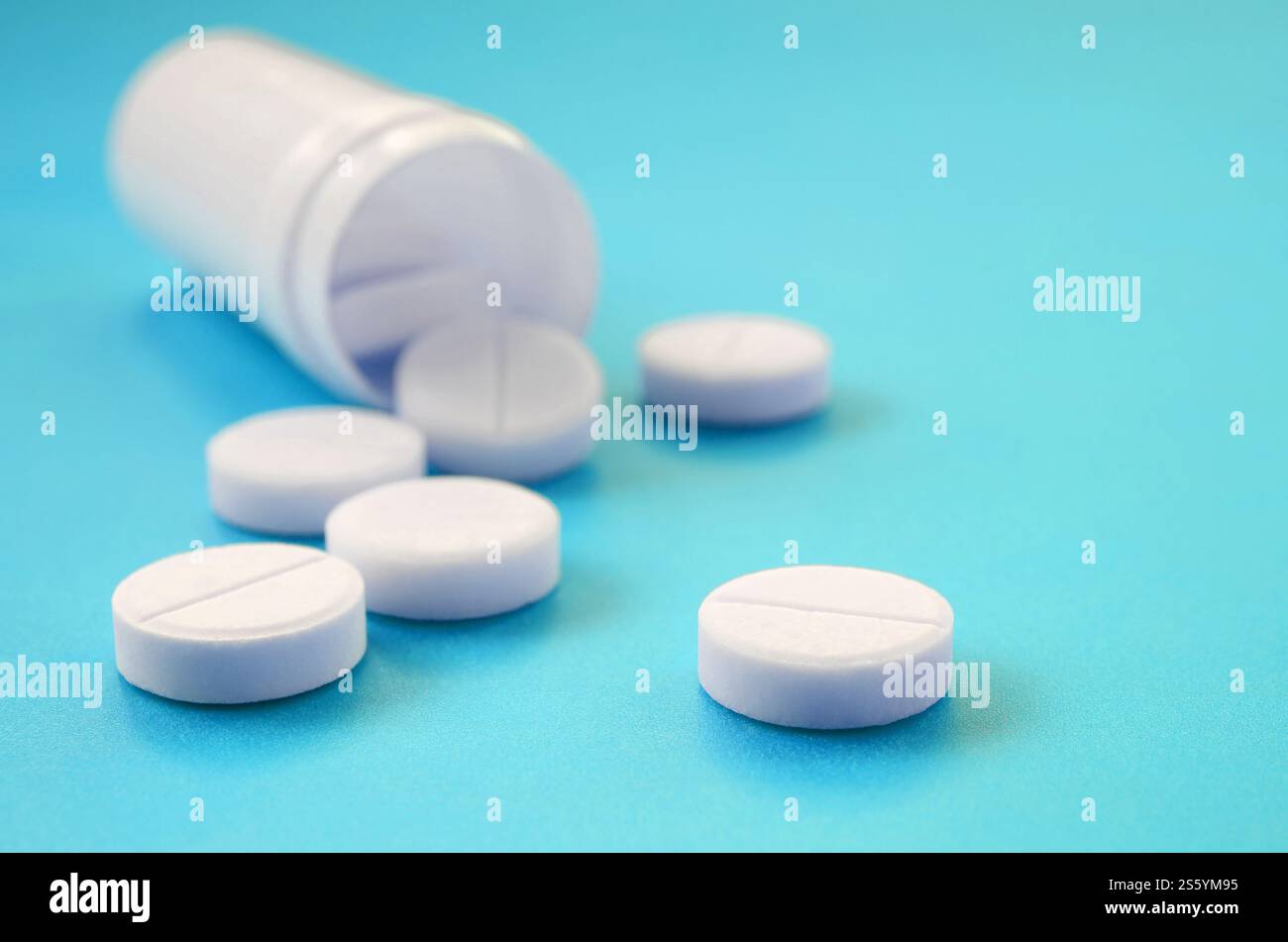 Mehrere weiße Tabletten fallen aus der Kunststoffbehälter auf der blauen Fläche. Hintergrundbild über medizinische und pharmazeutische Themen Stockfoto