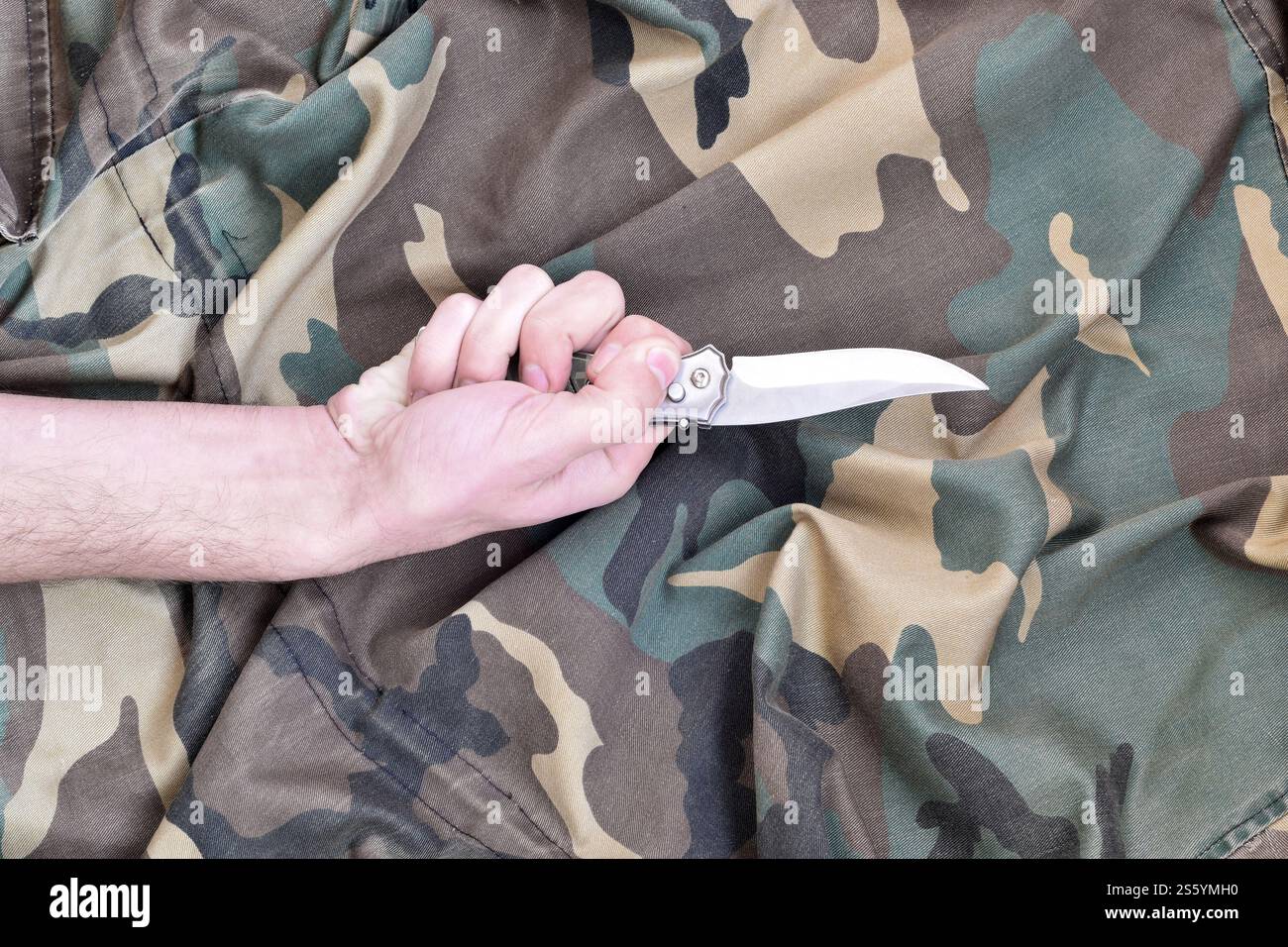 Hand mit kleinem Messer auf Tarnstoff Hintergrund. Das Konzept, ein Messer in Nahkampftaktiken beim Militär einzusetzen. Hand mit kleinem Messer auf Stockfoto