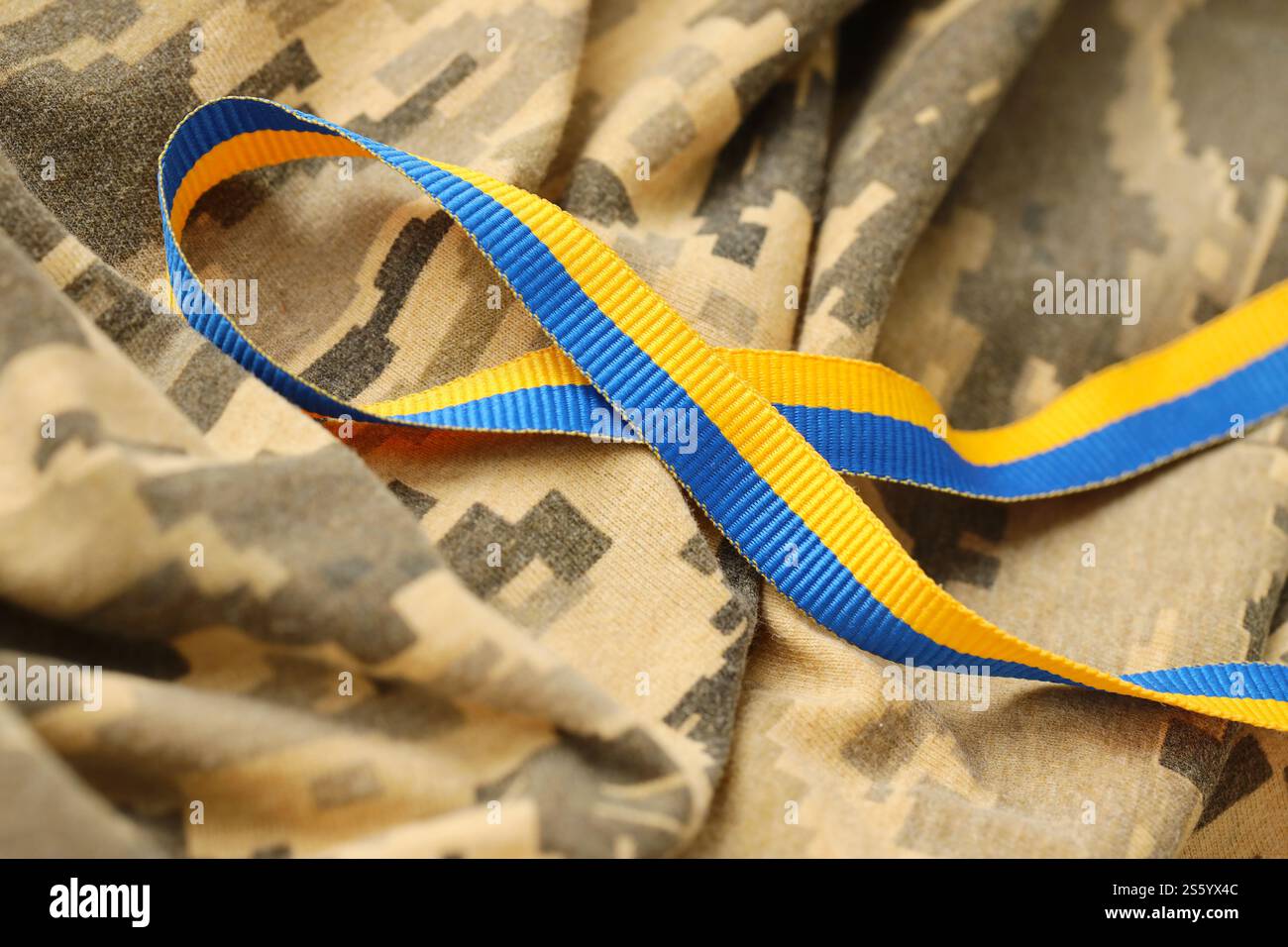 Gepixelter, digitaler Militärtarnstoff mit Band in blauen und gelben Farben. Attribute der ukrainischen patriotischen Soldatenuniform. Gepixelt digital Stockfoto