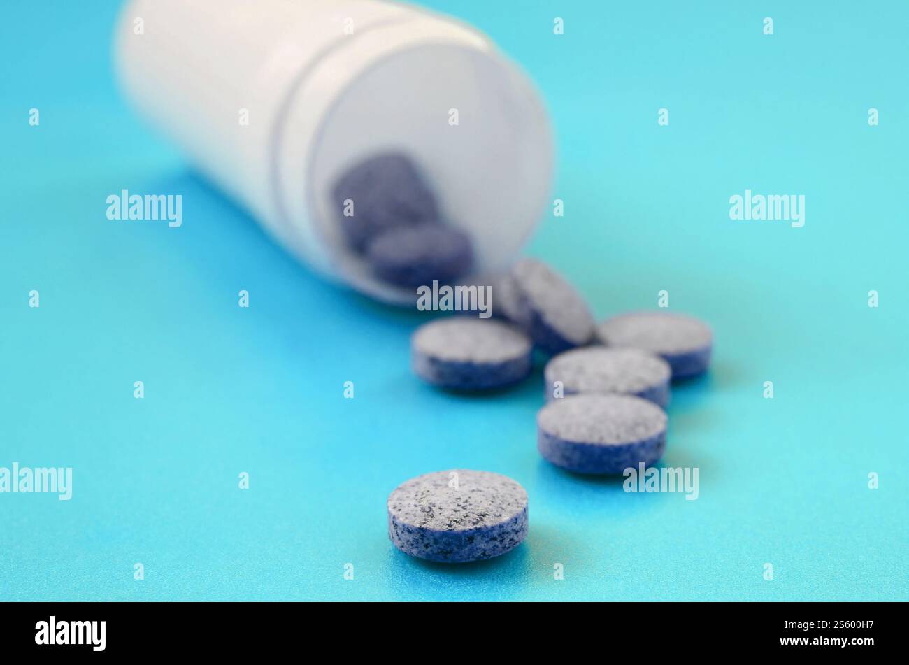 Mehrere graue Tabletten fallen aus der Kunststoffbehälter auf der blauen Fläche. Hintergrundbild über medizinische und pharmazeutische Themen Stockfoto