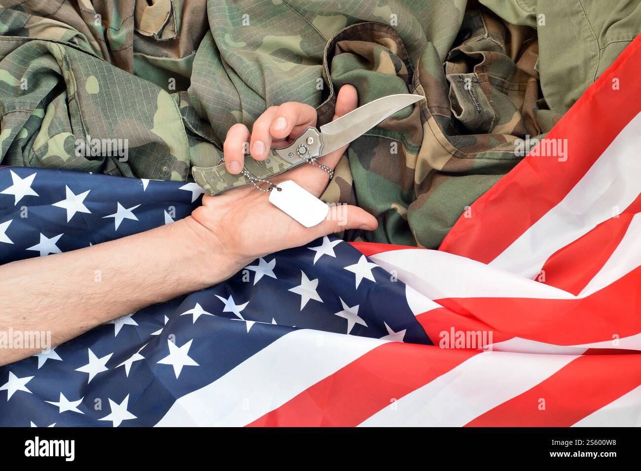 Hundemarken liegen bei der Hand eines Menschen, der Selbstmord mit einem Messer begeht. Das Konzept eines Veteranen, der den Schmerz nicht länger ertragen kann, beschließt, sich umzubringen. Hund Stockfoto