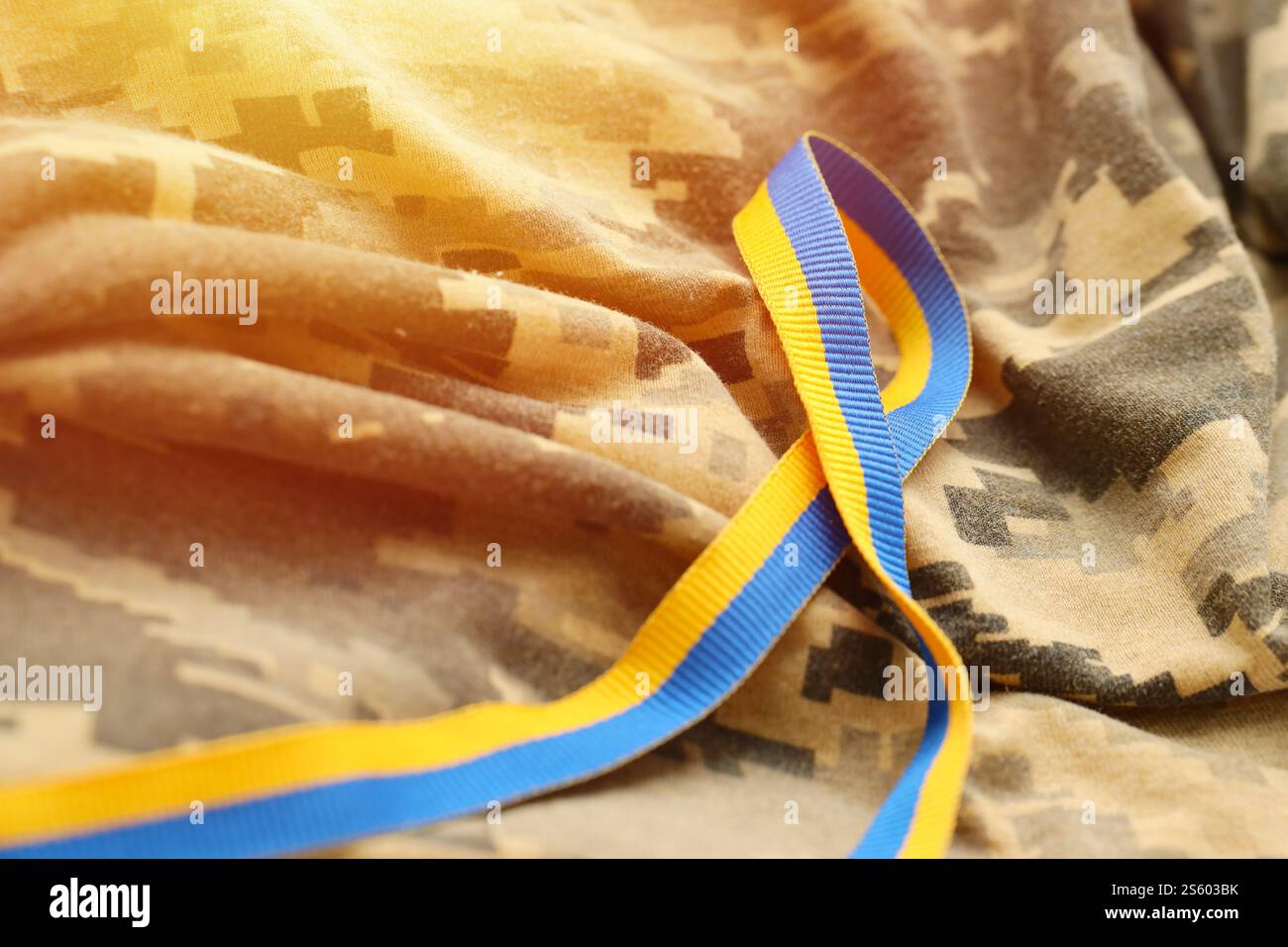Gepixelter, digitaler Militärtarnstoff mit Band in blauen und gelben Farben. Attribute der ukrainischen patriotischen Soldatenuniform. Gepixelt digital Stockfoto