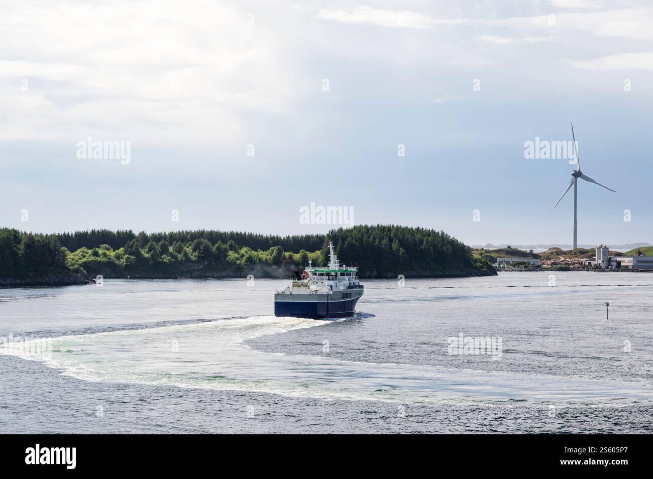 Ein Arbeitsboot, das vor der Küste Südnorwegens segelt, mit einer Windturbine am Ufer Stockfoto