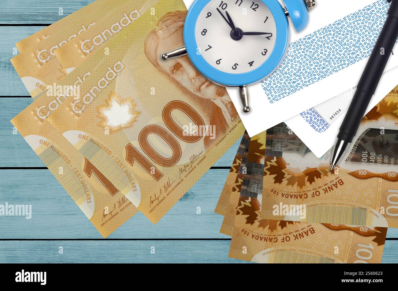 100 kanadische Dollar-Scheine und Wecker mit Stift und Umschlägen. Steuersaisonkonzept, Zahlungsfrist für Kredit oder Darlehen. Finanzoperationen Stockfoto