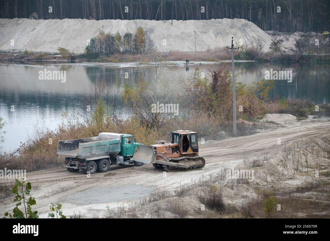 Caterpillar-Lader und Muldenkipper arbeiten im Tagebau. Schwere Maschinen in der offenen Grube am Fluss. Planierschild und Lkw beim Graben und Stockfoto