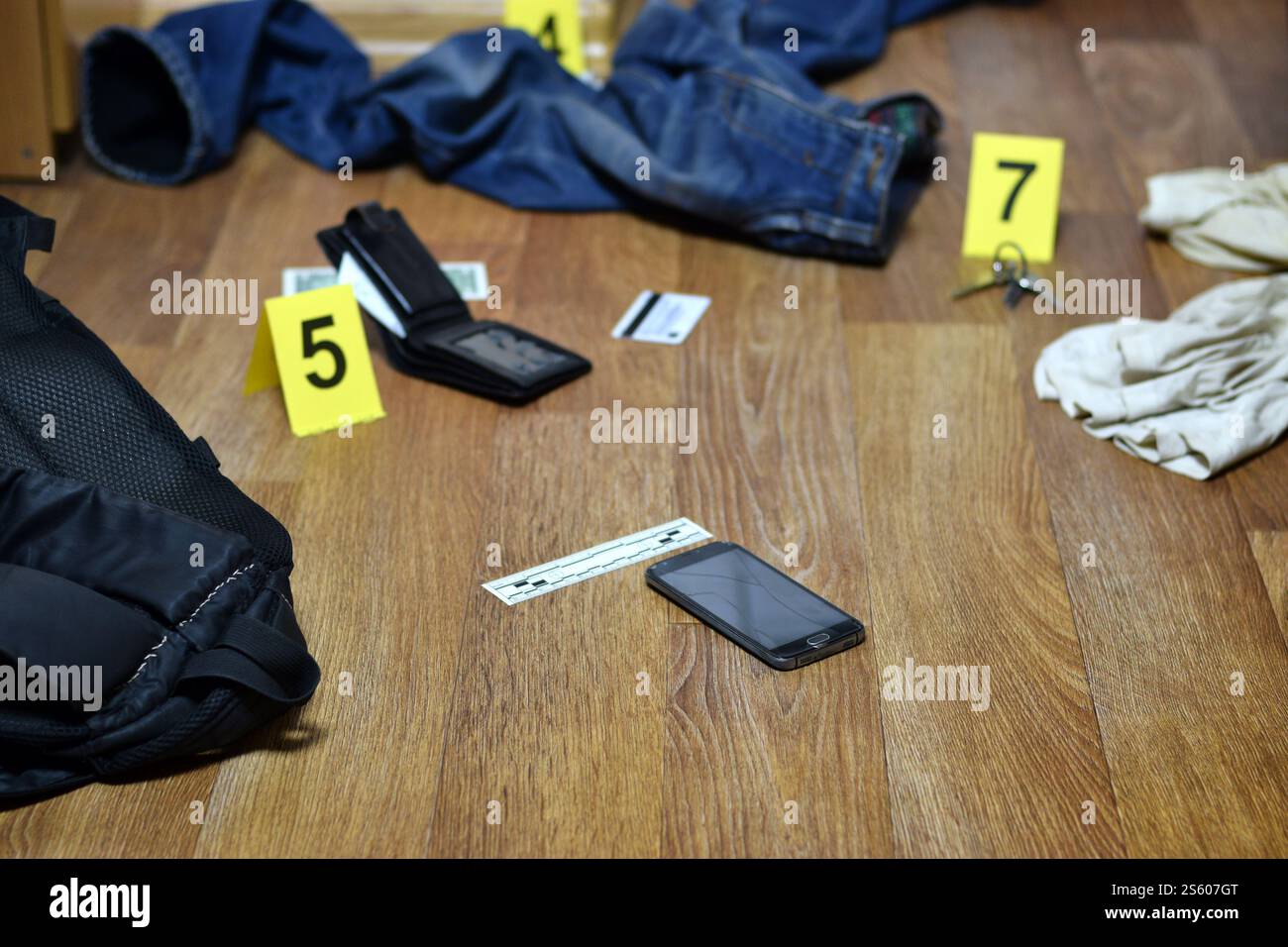 Tatortuntersuchung - Nummerierung der Beweise nach dem Mord in der Wohnung. Kaputtes Smartphone, Brieftasche und Kleidung mit Beweismarkierungen Stockfoto