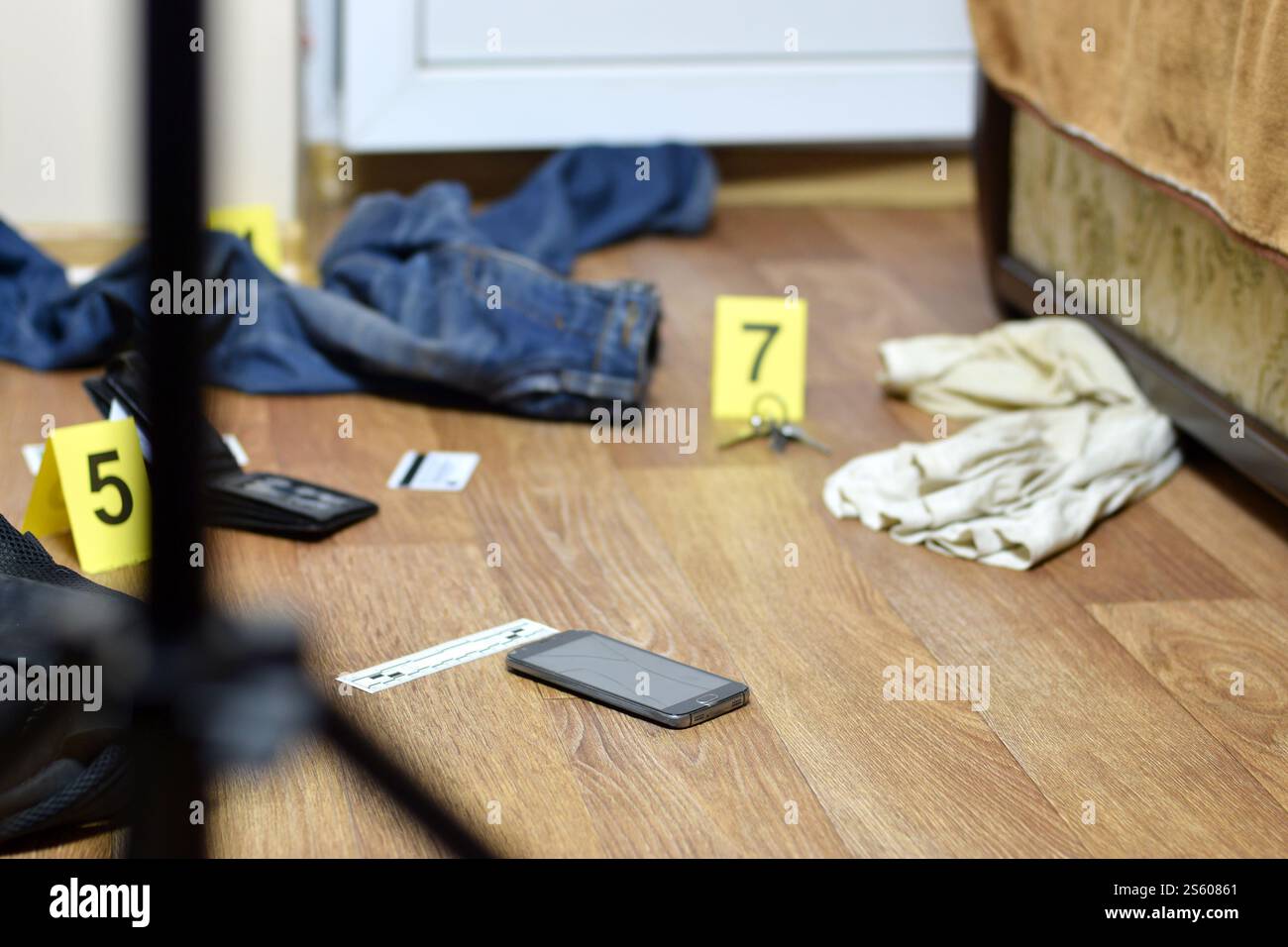 Tatortuntersuchung - Nummerierung der Beweise nach dem Mord in der Wohnung. Kaputtes Smartphone, Brieftasche und Kleidung mit Beweismarkierungen Stockfoto