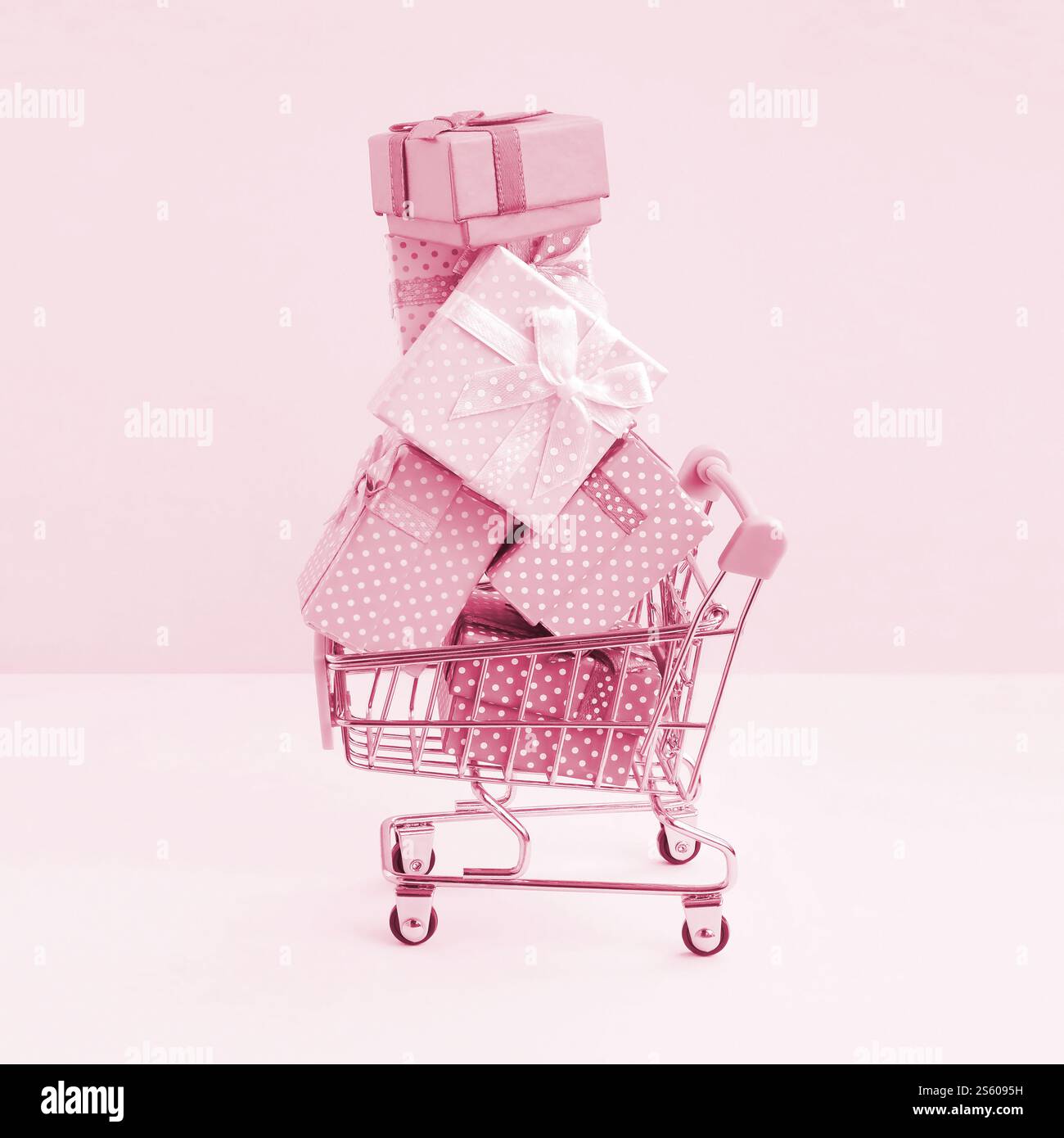 Viele bunte Geschenkboxen im Einkaufswagen des Supermarktes auf pfirsichfarbenem Hintergrund. Geschenke für Winterferien Bildton in Viva Magenta, Farbe des Stockfoto
