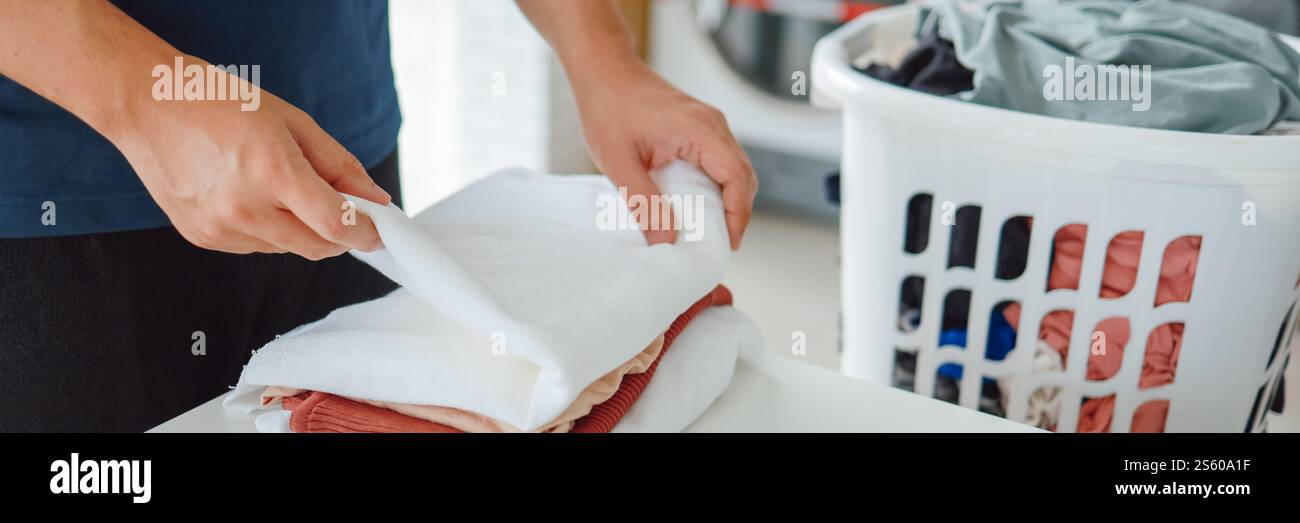 Hausmann mit Korb und schmutziger Wäsche gewaschene Kleidung im Waschraum. Waschmaschine im Wäschereigeschäft Konzept Stockfoto