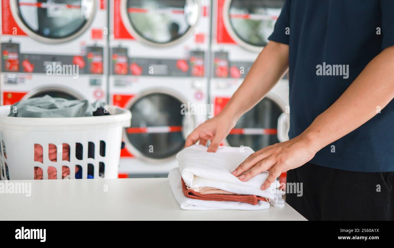 Hausmann mit Korb und schmutziger Wäsche gewaschene Kleidung im Waschraum. Waschmaschine im Wäschereigeschäft Konzept Stockfoto