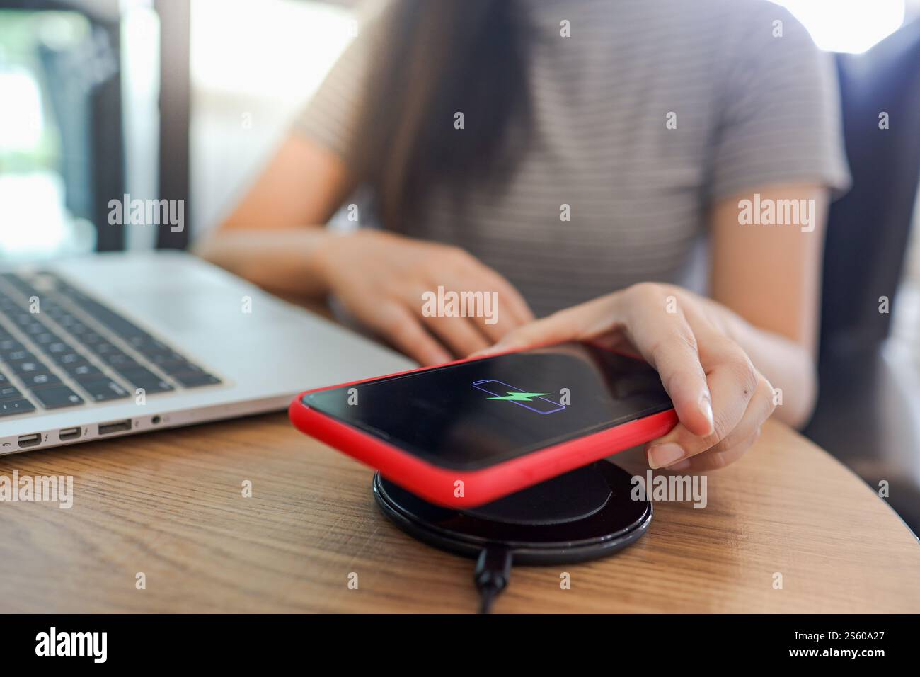 Laden des Mobiltelefonakkus mit dem drahtlosen Gerät in der Tabelle. Smartphone wird auf einem Ladepad aufgeladen. Mobiltelefon in der Nähe des kabellosen Ladegeräts Stockfoto