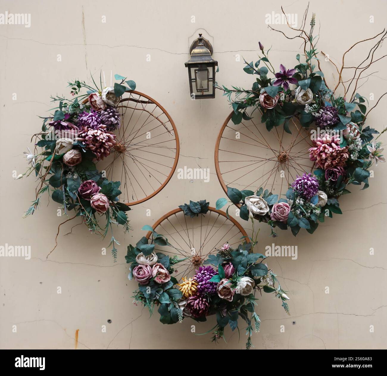 Dekoration urbanes Kunstobjekt von Fahrradrädern und farbenfrohe, elegante Blumen an der Wand. Dekoration urbanes Kunstobjekt von Fahrradrädern und Blumen auf Stockfoto