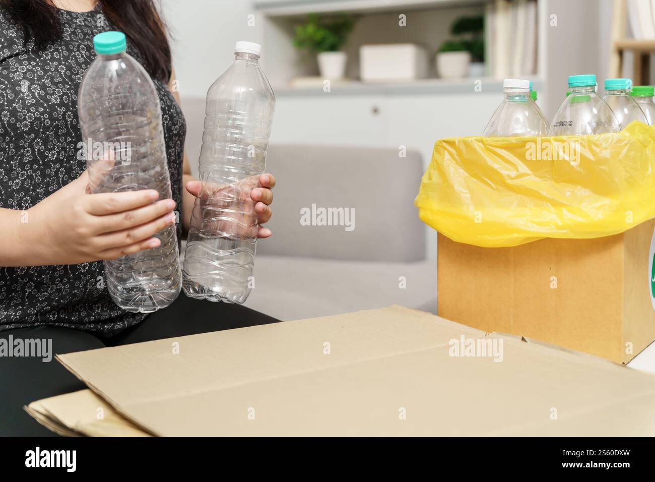 Recyceln Sie die umweltfreundliche Zero Concept Frau, die leere Plastikflasche mit gelben Mülltüten zu Hause in den Recyclingbehälter wirft Stockfoto