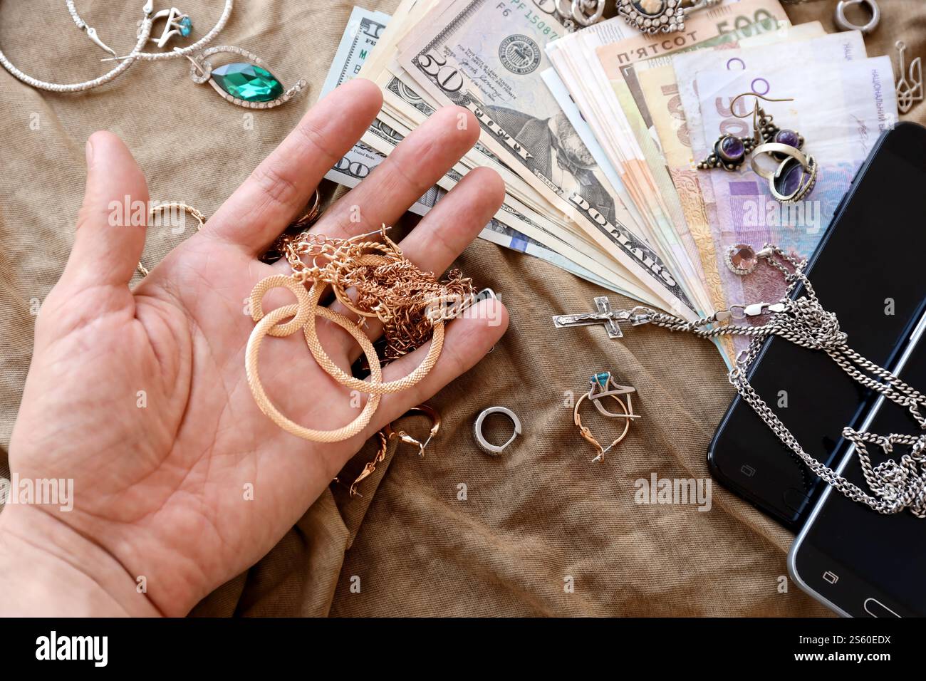 Marodeure tragen einen Haufen gestohlenen Schmuck, Geld und Smartphones auf Militäruniform Stoff. Plünderung durch russische Soldaten in der Ukraine Stockfoto