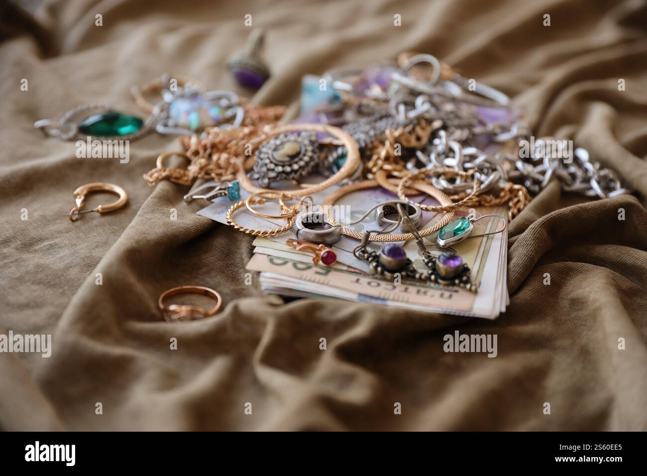 Ein Haufen gestohlener Schmuck und Geld auf Militäruniform Stoff. Plünderung durch russische Soldaten in den ukrainischen Städten während des russischen Angriffs auf Stockfoto